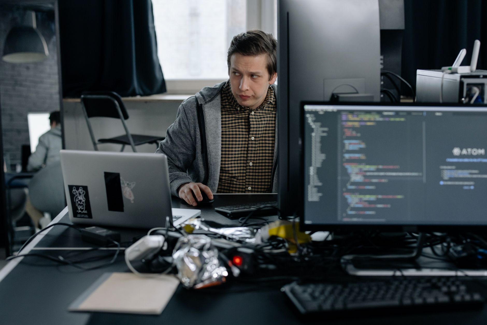 Un homme assis devant un bureau d’ordinateur avec du code informatique affiché sur les écrans.
